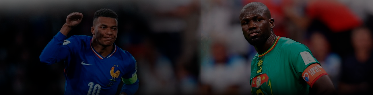 На изображении два футболиста: слева игрок в синей форме команды Франции, справа игрок в зелёной форме команды Камеруна. Они находятся на поле, фон размытый, с видимыми зрителями