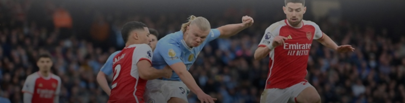 Футбольный матч: игрок в голубой форме ведёт борьбу с двумя соперниками в красно-белой экипировке на фоне стадиона. Интенсивный момент игры