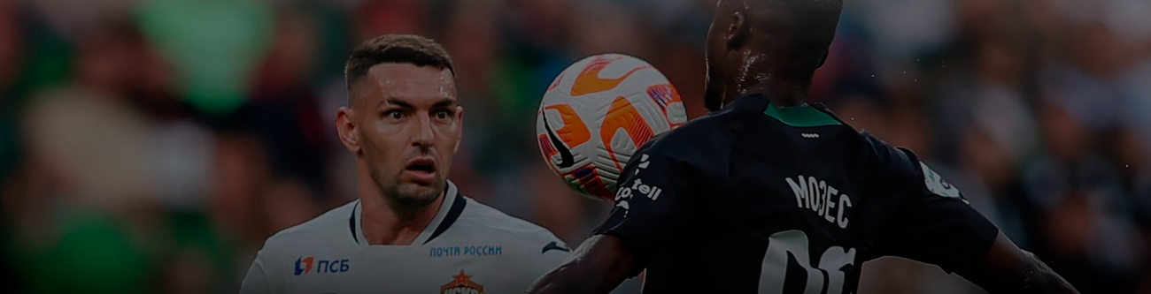 Футболист в белой форме смотрит на мяч, который контролирует соперник в черно-зеленой форме. Стадион заполнен зрителями